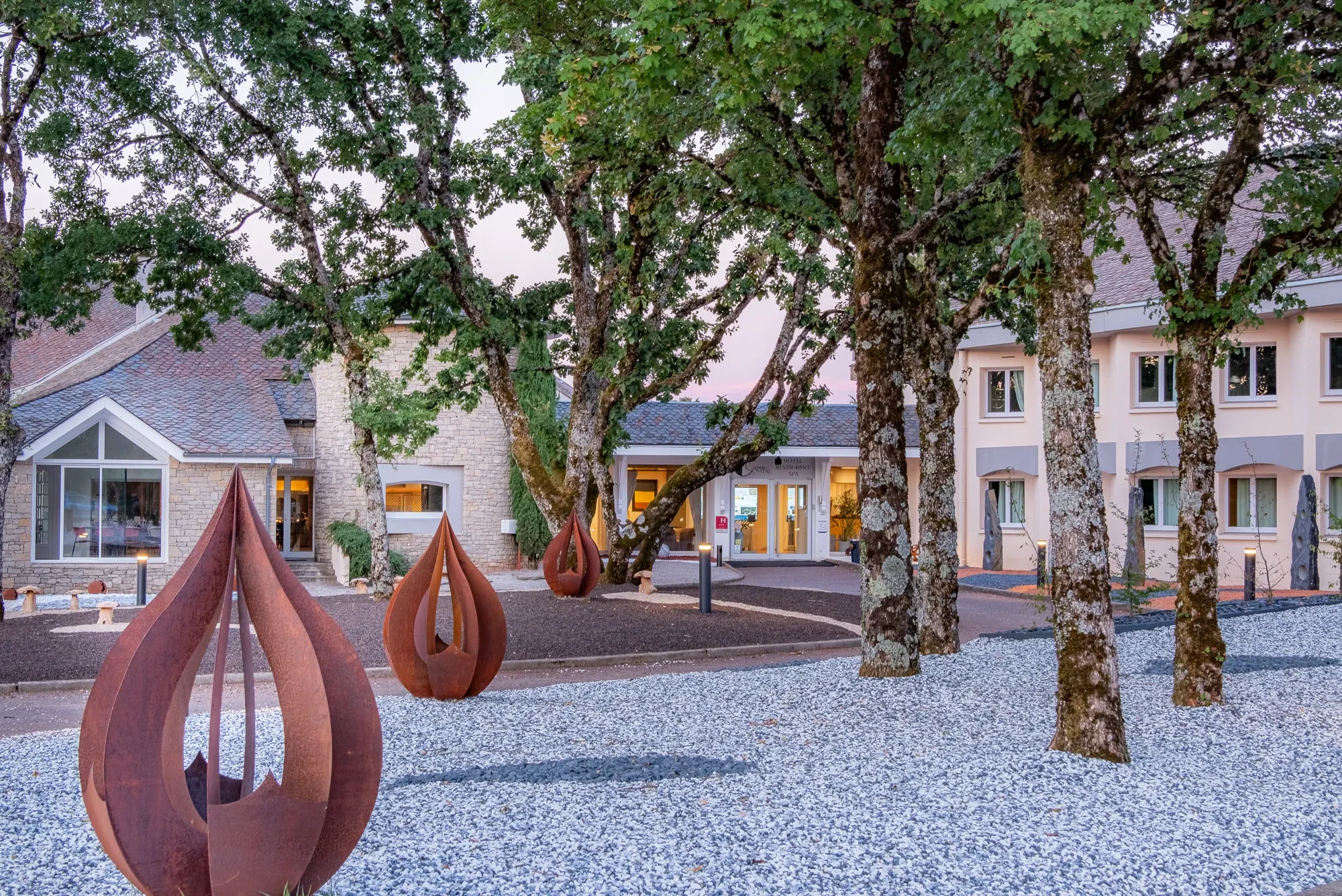Entrée d’un hôtel entourée d’arbres et sculptures.