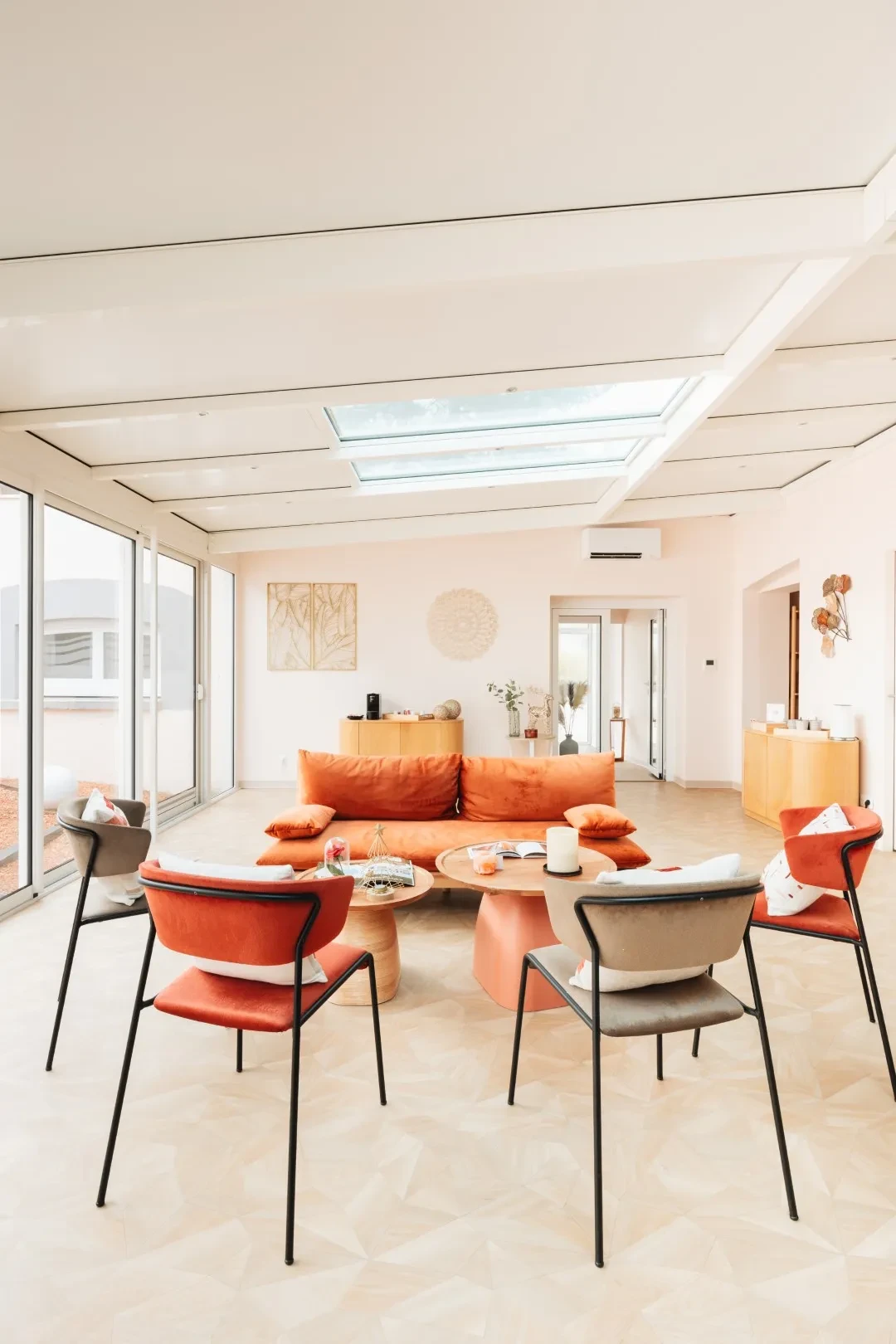 Salon lumineux avec canapé orange et grandes fenêtres