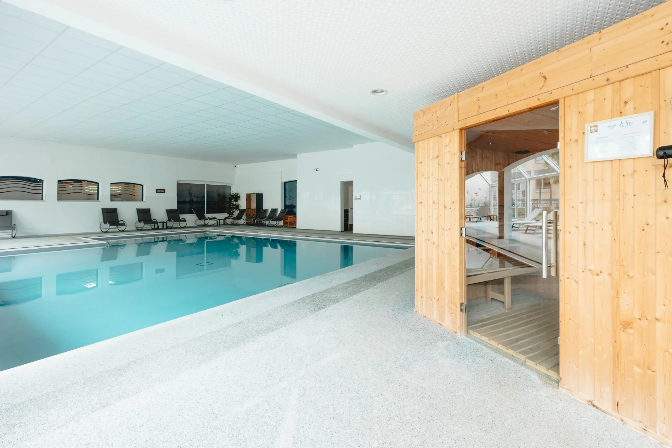 Piscine intérieure avec sauna en bois et transats.